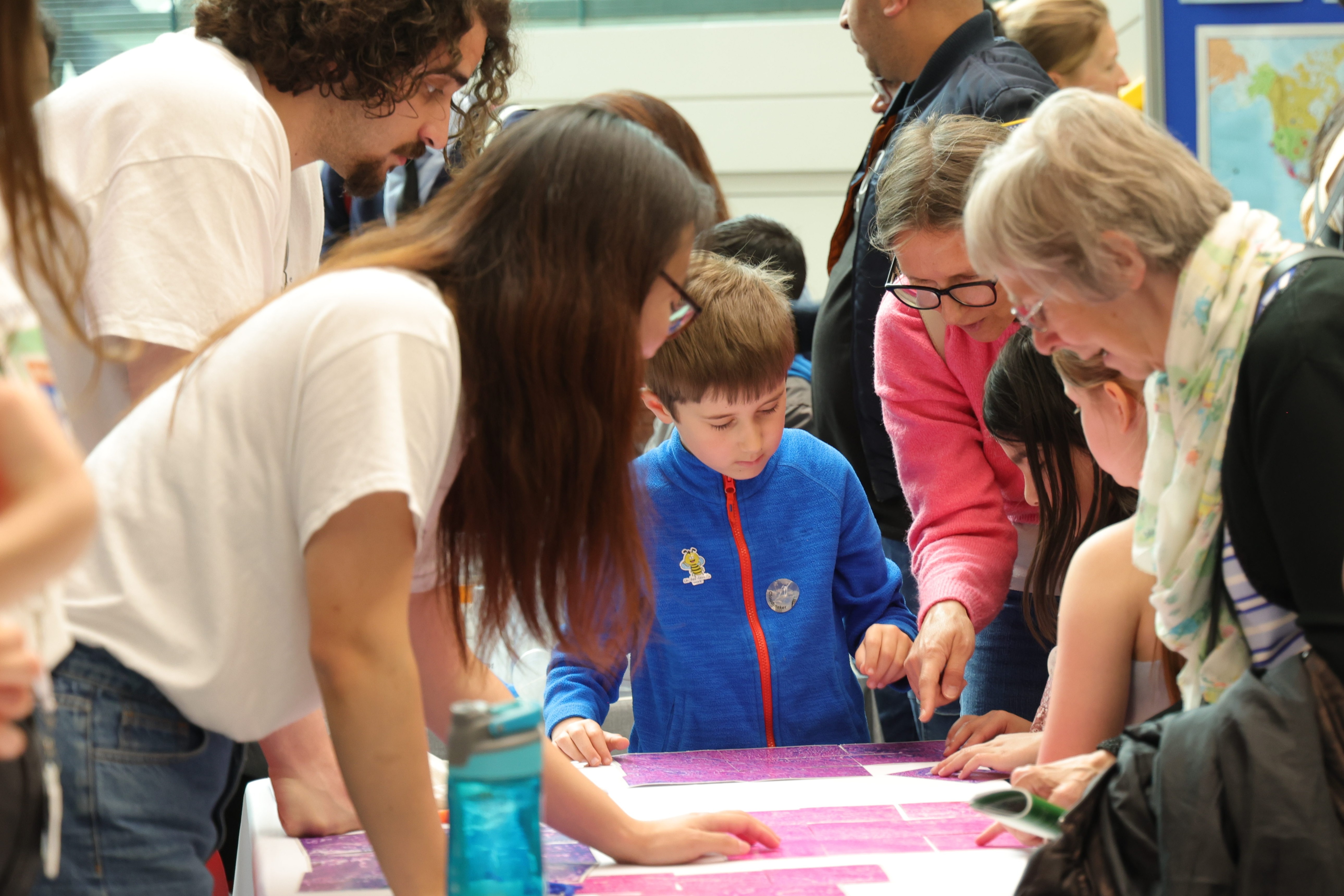 Child in focus in the middle doing a jigsaw puzzle of a histology slide with adults around the table looking down